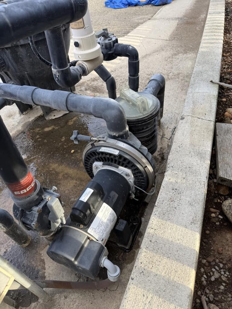 Pool pump and filter system with interconnected PVC pipes in a concrete pool equipment pit.