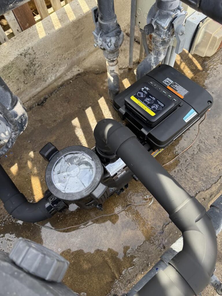 Outdoor pool pump and filtration system with black motor and PVC piping in a concrete utility pit.
