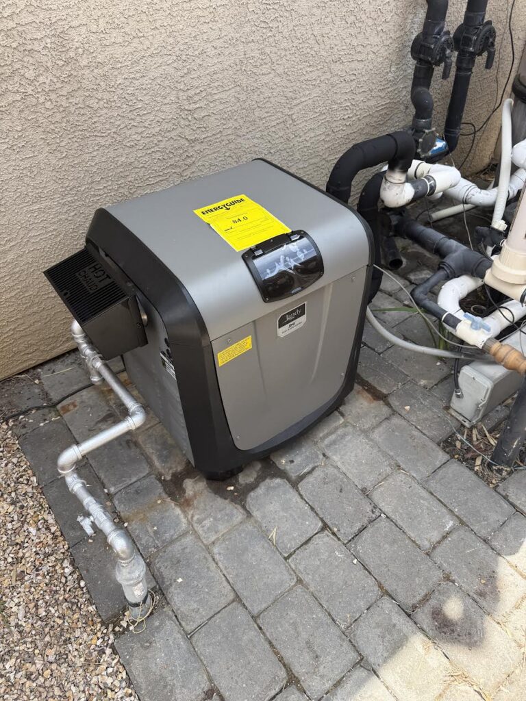 Outdoor pool heat pump unit attached to a stucco wall, with exposed silver and black pipes and a yellow EnergyGuide label on top.